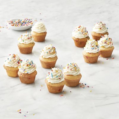 Mini muffins à la vanille avec glaçage à la crème et bonbons colorés, disposés sur un comptoir de marbre