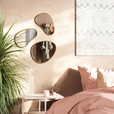 Ensemble de trois miroirs muraux organiques à cadre doré de chez Kozy, décorant une chambre douce aux tons rosés avec plante verte et table de chevet blanche.