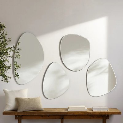 Quatre miroirs muraux organiques de chez Lovaco disposés de façon asymétrique au-dessus d'une console en bois avec coussins décoratifs.