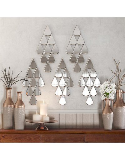 Miroirs muraux en forme de gouttes assemblés en motif de sapin de chez Ô Miroir, décorant un mur au-dessus d’un buffet en bois avec vases et chandelles.