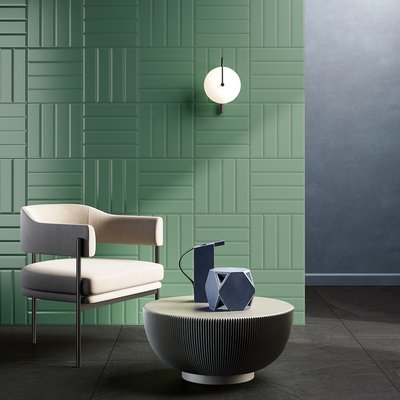 Mur accent vert sauge avec revêtement mural texturé en céramique aux motifs géométriques, chaise moderne beige au design épuré, table basse ronde striée avec objets décoratifs bleus et ambiance contemporaine minimaliste par Déco Surfaces.