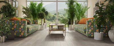 Salon lumineux avec plancher de bois franc gris pâle de la collection Arabelle de Fuzion Flooring, meubles colorés et vue panoramique sur la nature.