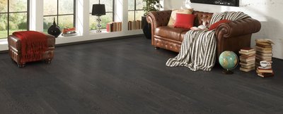 Salon élégant avec plancher de bois franc foncé Barn Barrel de Fuzion Flooring, canapé en cuir brun et décoration vintage.
