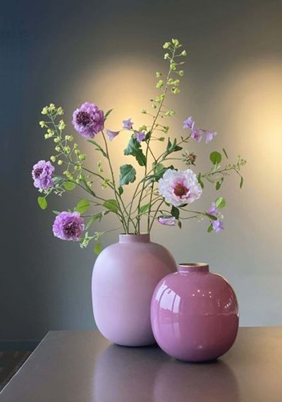 Deux vases en céramique rose, l'un mat et l'autre brillant, contenant un arrangement floral composé de fleurs violettes et blanches avec feuillage vert, posés sur une table dans un décor contemporain Source - Beskrajne mudrosti Pinterest