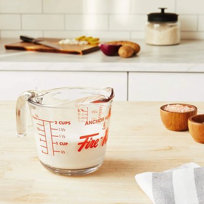 Bol à mesurer en verre Anchor Hocking Fire-King avec graduations rouges, posé sur un comptoir de cuisine en bois clair – Accessoire de précision pour mesurer liquides, offert par La Guilde Culinaire