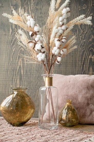Décoration intérieure avec bouquet de coton et herbes séchées dans un vase en verre transparent, accompagné de vases dorés et d'un coussin rose pâle sur fond de bois naturel chez décors véronneau