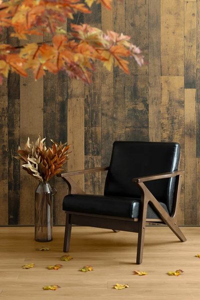 Fauteuil en bois foncé avec coussins noirs sur plancher de bois clair, décoré de feuilles d'automne, d'un vase en métal rempli de feuillage séché et d'un mur accent en bois rustique par Décors Véronneau