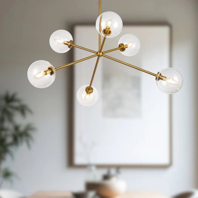 Chandelier Cassia suspendu au style moderne de chez Luminaires & Cie, composé de six globes en verre transparent fixés à une structure en métal doré brossé, dans une salle à manger contemporaine au décor minimaliste et chaleureux