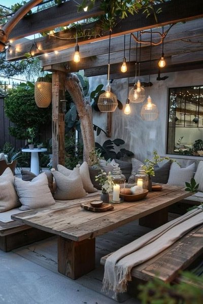 Terrasse extérieure de style bohème avec grande table en bois, coussins beiges et éclairage suspendu chaleureux sous une pergola Source - ΛCIDOΛZUCΛROSO Pinterest