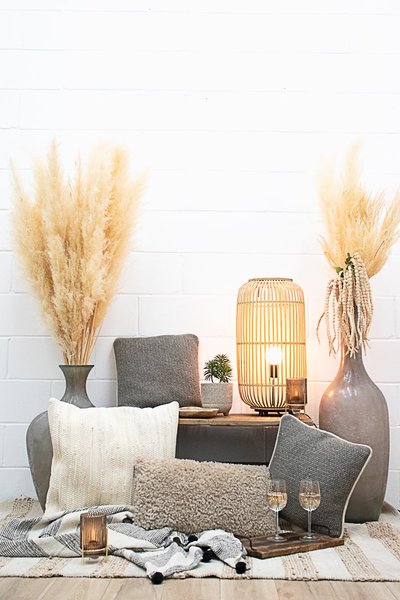 Décor intérieur de style bohème chic avec coussins texturés, vases en céramique, pampas séchées, lanterne en rotin, jeté à motifs et verres de vin sur plateau en bois chez décors véronneau