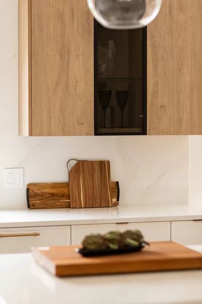 Gros plan d’un coin de cuisine signé Ateliers Jacob, mettant en valeur des armoires en bois clair avec porte vitrée centrale noire, comptoir en quartz blanc, planche à découper en bois naturel et plateau décoratif