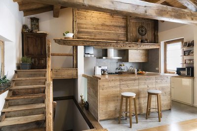 Cuisine champêtre en bois naturel signée Rénovilla, avec poutres apparentes, armoires rustiques, électroménagers encastrés et îlot central avec tabourets en bois, dans un décor chaleureux de style chalet