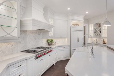 Cuisine contemporaine blanche conçue par Rénovilla, avec armoires sur mesure, hotte décorative, dosseret en chevrons de marbre, grand îlot avec robinet professionnel et comptoirs en quartz blanc