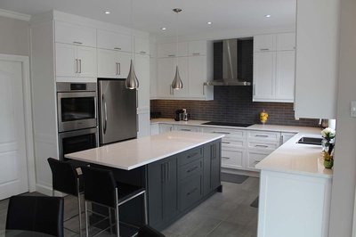 Cuisine contemporaine au style épuré par Rénovilla, avec armoires blanches shaker, dosseret en briques de céramique noires, hotte en acier inoxydable, îlot central noir charbon avec comptoir en quartz blanc et luminaires suspendus chromés