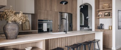 Cuisine contemporaine avec armoires en bois clair, îlot central avec comptoir en quartz beige et évier encastré noir, électroménagers encastrés en acier inoxydable, étagères ouvertes décorées et éclairage suspendu moderne noir mat, conçue par Armoires Cuisines Action