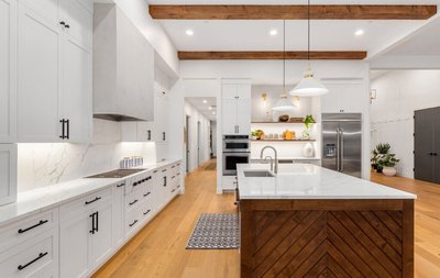 Cuisine blanche moderne signée Onivo avec armoires shaker, îlot central en bois en chevron avec comptoir en quartz, électroménagers en inox, hotte encastrée et poutres de bois au plafond