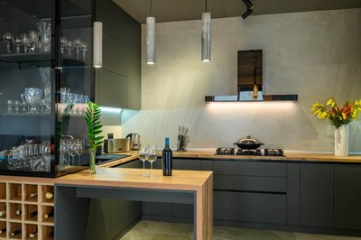 Cuisine contemporaine Onivo aux armoires foncées mat, comptoirs en bois naturel, cellier intégré, étagère vitrée pour verres, éclairage suspendu minimaliste et mur de finition en béton lisse