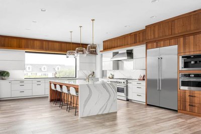 Cuisine moderne haut de gamme conçue par Onivo, avec armoires blanches et en noyer, grand îlot central en quartz aux veinures grises, électroménagers encastrés en inox, luminaires suspendus en verre et plancher effet bois clair