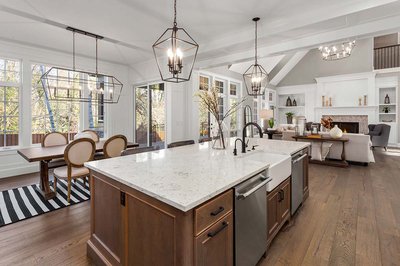 Cuisine classique par Rénovilla avec îlot central en bois foncé et comptoir en quartz, robinetterie noire mat, luminaires suspendus géométriques, coin repas avec table rustique et chaises rembourrées, ouverte sur un salon avec foyer encastré et plafond cathédrale