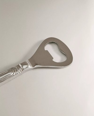 Décapsuleur en acier inoxydable avec manche sculpté de style classique, posé sur une surface neutre – produit Zara Home