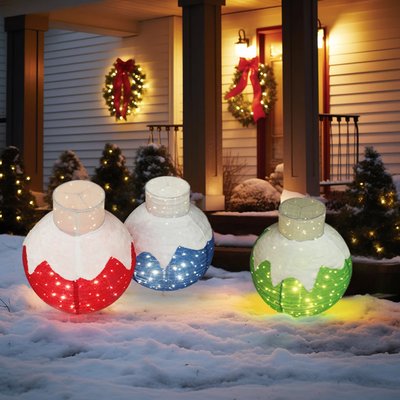 Trois décorations extérieures lumineuses en forme de boules de Noël rouge, bleue et verte, installées dans la neige devant une maison décorée pour les fêtes - Wayfair