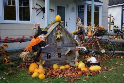 Décoration extérieure d'Halloween devant une maison avec des sorcières sur balai, une petite cabane en bois, des citrouilles, des feuilles d'automne et un vieux vélo décoré.