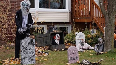 Cour avant décorée pour l'Halloween avec un loup-garou, des pierres tombales, un clown terrifiant, des zombies et des squelettes devant une maison.