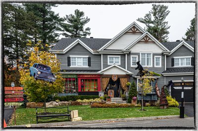Maison décorée pour l'Halloween sur le thème d'Harry Potter, avec voiture volante, pancartes de Poudlard, sorcières, balais et devanture de boutique magique.