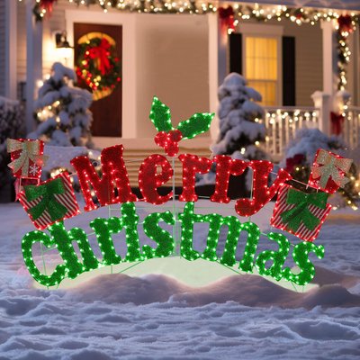 Enseigne lumineuse extérieure 'Merry Christmas' en rouge et vert avec décorations de cadeaux et houx, placée sur la neige devant une maison décorée pour Noël - Wayfair