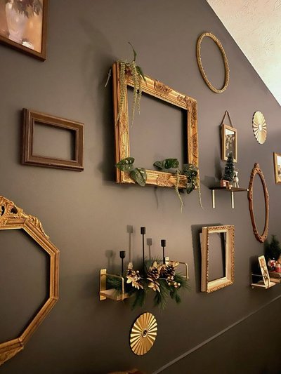 Mur foncé décoré de cadres dorés et anciens, certains vides ou ornés de plantes suspendues, créant une composition murale artistique et éclectique Source - Eclectic Home Pinterest