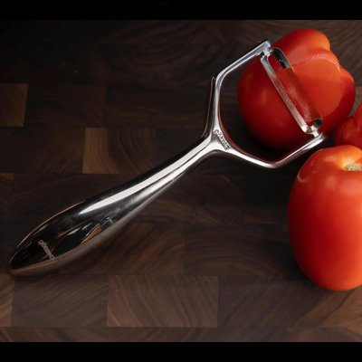 Éplucheur Deluxe en acier inoxydable de Eugène Allard, utilisé pour peler une tomate mûre sur une planche en bois