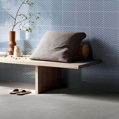 Mur de céramique bleue à motifs d’écailles blanches dans un espace de détente minimaliste, banc en bois naturel décoré de coussins et d’objets en céramique artisanale, sur un plancher de tuiles grises modernes par Déco Surfaces.