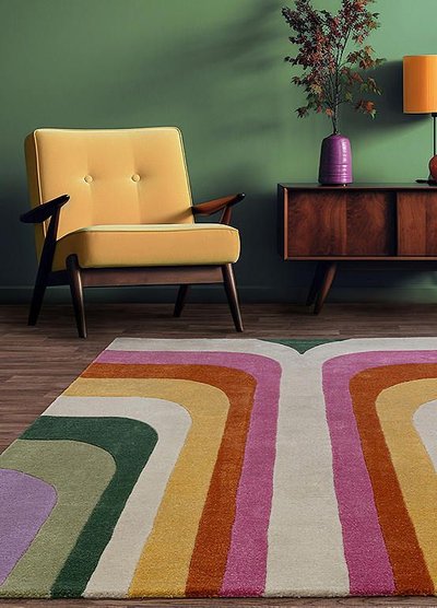 Intérieur rétro coloré avec fauteuil jaune, mur vert, tapis à motifs courbes multicolores et meuble bas en bois foncé de style vintage Source - Freemans Online Pinterest