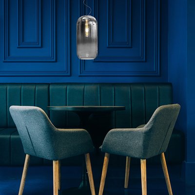 Coin repas chic avec mur bleu profond, banquette capitonnée, deux chaises modernes et luminaire suspendu Gople en verre fumé de Maison du Luminaire