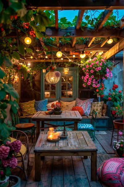 Terrasse éclectique et fleurie sous pergola en bois, décorée de guirlandes lumineuses Source - Home, Garden Lighting and Gardening Pinterest Terrasse éclectique et fleurie sous pergola en bois, décorée de guirlandes lumineuses, coussins colorés, lanternes suspendues et plantes abondantes, créant une ambiance bohème et festive en soirée Source - Home, Garden Lighting and Gardening Pinterest