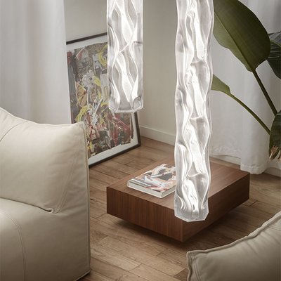 Suspensions design Hugo Vertical de Slamp émettant une lumière sculpturale dans un salon moderne avec fauteuils crème, plante tropicale et table basse en bois – Maison du Luminaire