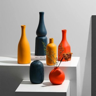 Ensemble de vases modernes aux formes minimalistes et aux couleurs vives - orange, jaune et bleu - exposés sur des socles blancs dans un décor contemporain Source - Jievik Pinterest
