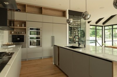 Cuisine moderne haut de gamme signée Ateliers Jacob, avec armoires gris mat pleine hauteur, électroménagers encastrés en inox, îlot central avec évier noir, comptoir en quartz blanc et suspensions sphériques chromées dans un espace lumineux à aire ouverte