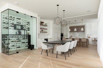 Vue d’ensemble d’une cuisine haut de gamme conçue par Ateliers Jacob avec îlot central blanc, chaises rembourrées beiges, salle à manger attenante avec table noire et chaises grises, cave à vin vitrée encastrée et éclairage suspendu au design géométrique