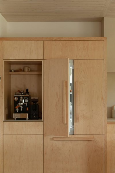 Coin café intégré dans une cuisine en bois clair de style épuré signée Ateliers Jacob, avec machine à espresso professionnelle encastrée, armoires pleine hauteur au design minimaliste et réfrigérateur dissimulé derrière des panneaux en bois assortis
