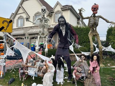 Cour avant décorée pour l'Halloween avec squelettes géants, mannequins effrayants, toiles d'araignée, citrouilles et personnages d'horreur devant une maison.