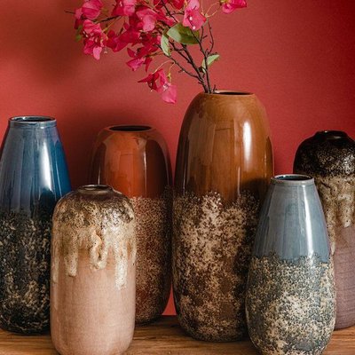 Ensemble de vases en céramique émaillée aux tons naturels et texturés, ornés de dégradés de brun, bleu et beige, avec fleurs roses dans l'un d'eux, sur fond rouge Source - La Redoute Pinterest