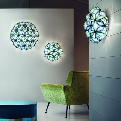 Murale artistique rétroéclairée La Vie de Slamp, aux motifs floraux géométriques bleu-vert, illuminant un salon moderne avec fauteuil vert lime – Maison du Luminaire