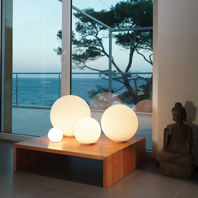 Ensemble de lampes de table sphériques diffusant une lumière chaude, disposées sur une table basse en bois près d'une baie vitrée avec vue sur la mer, photo par Luminaires & cie