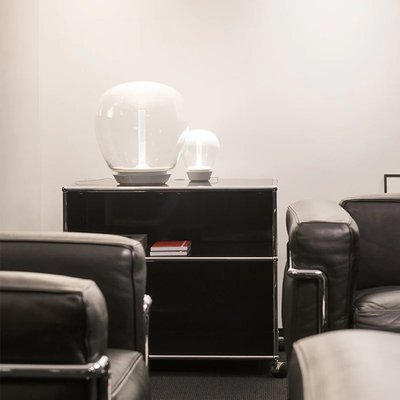 Deux lampes de table en verre blanc au design minimaliste, posées sur un meuble noir dans un salon contemporain, photo par Luminaires & cie