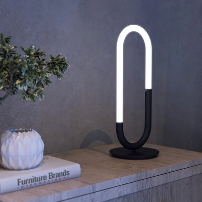 Lampe de table moderne en forme de boucle lumineuse avec base noire, posée sur un meuble en bois clair, photo par Luminaires & cie