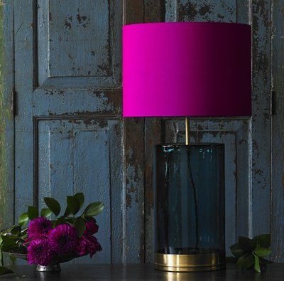 Photo par Jessica Knight Lampe de table avec pied en verre fumé et abat-jour cylindrique fuchsia, posée devant une porte en bois vieilli, Image Pinterest