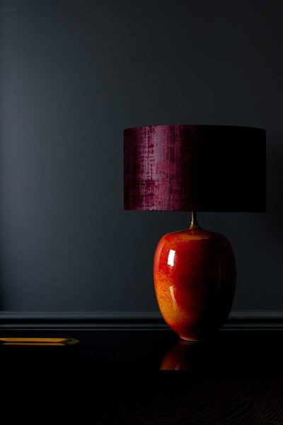 Lampe de table avec pied en céramique rouge orangé et abat-jour cylindrique bordeaux, posée sur une surface noire, image Pinterest