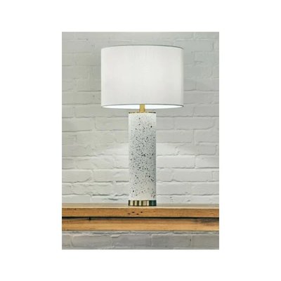 Lampe de table moderne de couleur blanche avec pied cylindrique en terrazzo et base dorée, abat-jour rond en tissu blanc, posée sur une étagère en bois devant un mur de briques peint en blanc, image provenant de Royaume Luminaire