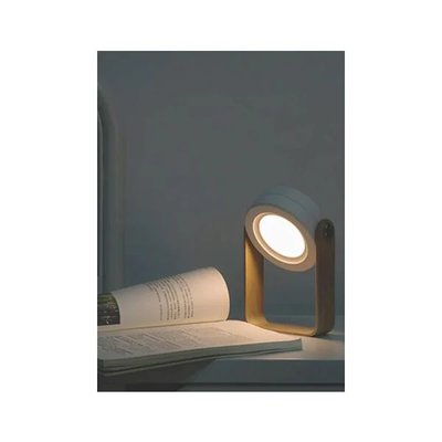 Lampe de table design minimaliste avec structure en bois clair et projecteur circulaire orientable, utilisée comme lumière de lecture sur une table avec un livre ouvert, image provenant de Royaume Luminaire